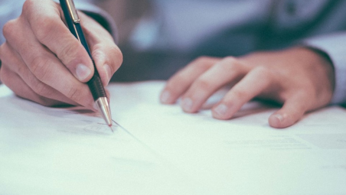A person signing a legal notice at a desk, pen in hand